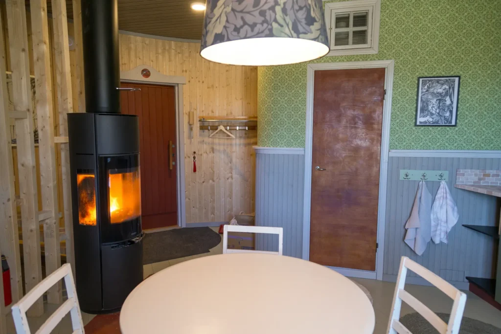 Keittiö, josta näkyy kylpyhuoneen ovi, ruokapöytä ja takka. 